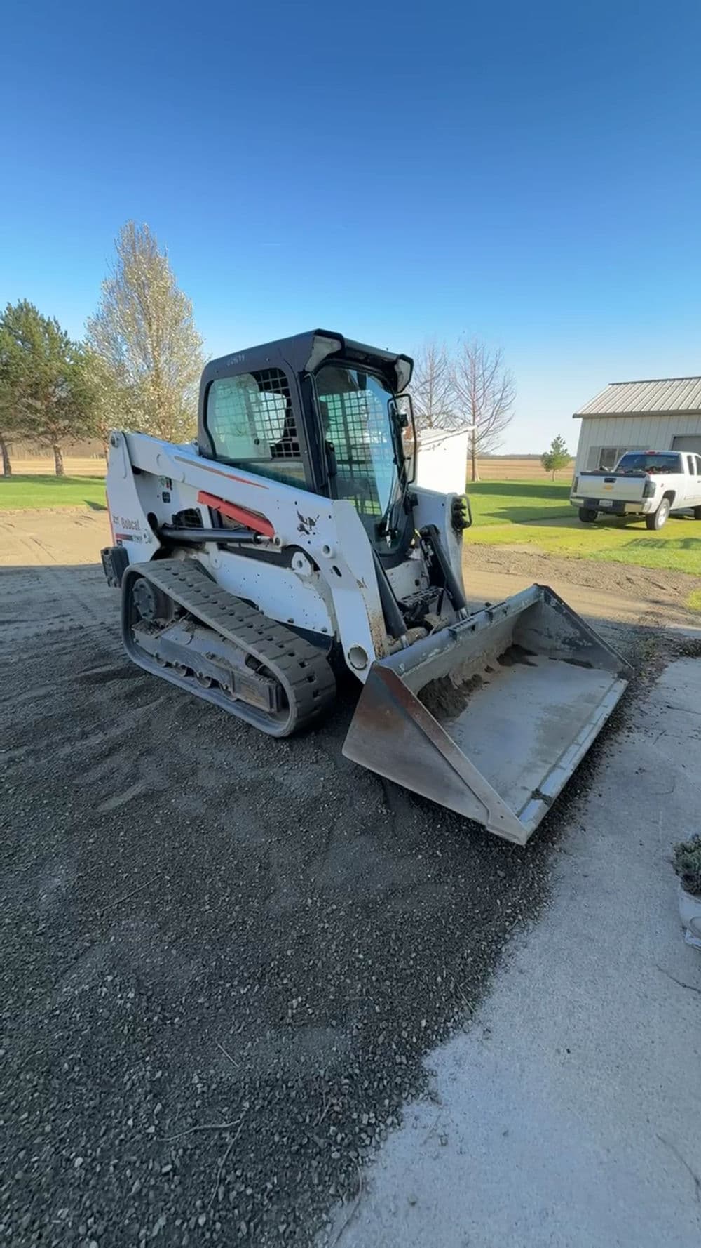 Bobcat skid steer loader on gravel with clear blue sky and parked truck in background.
