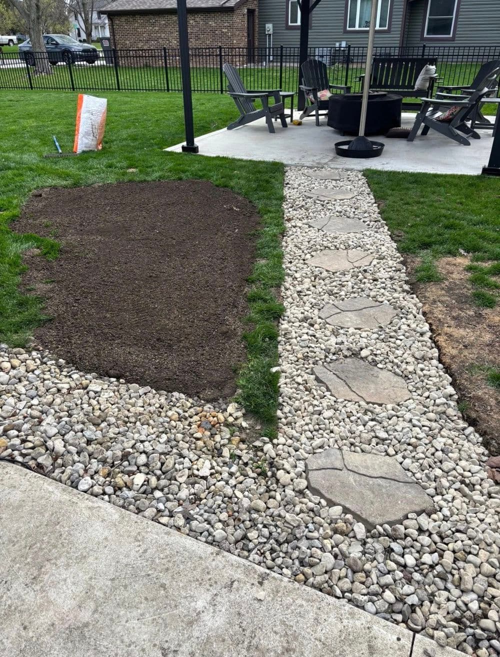 Garden pathway with stone steps and gravel border alongside freshly prepared soil area.