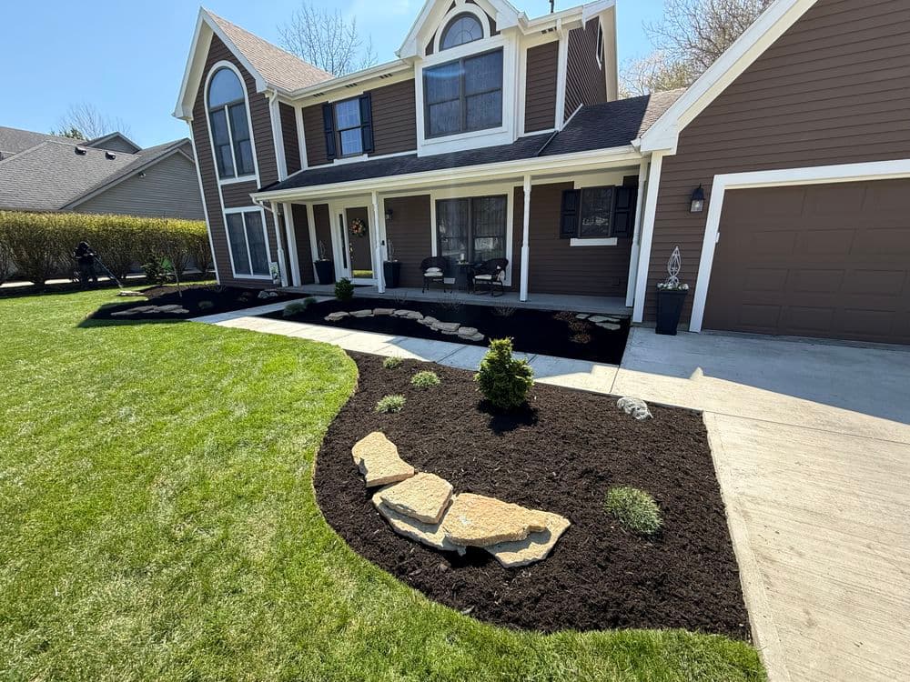 Front yard landscaping featuring mulch, stone paths, and green grass around a two-story home.
