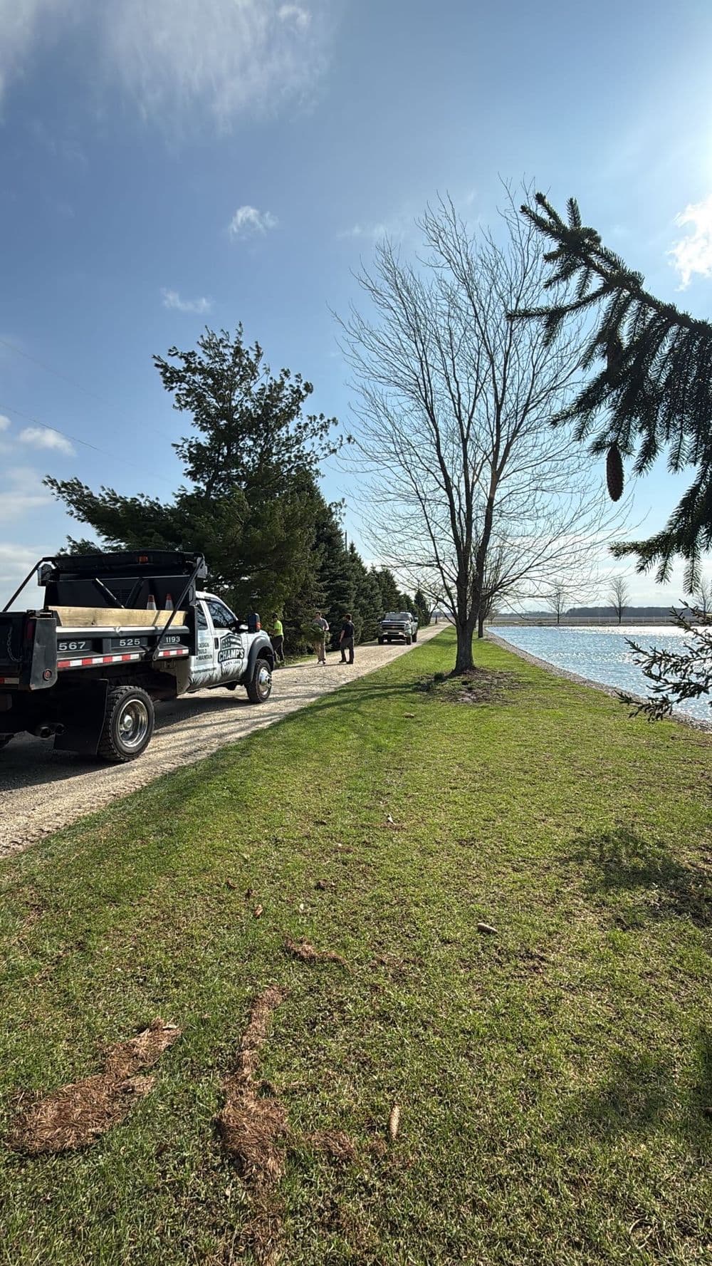 Utility truck parked by a lakeside path, surrounded by trees and a clear blue sky.