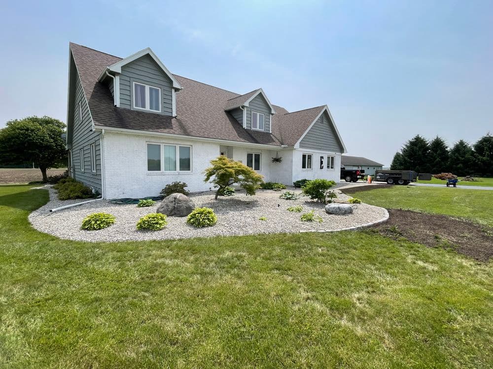 Two-story house with landscaped yard and gravel garden, under clear blue sky.
