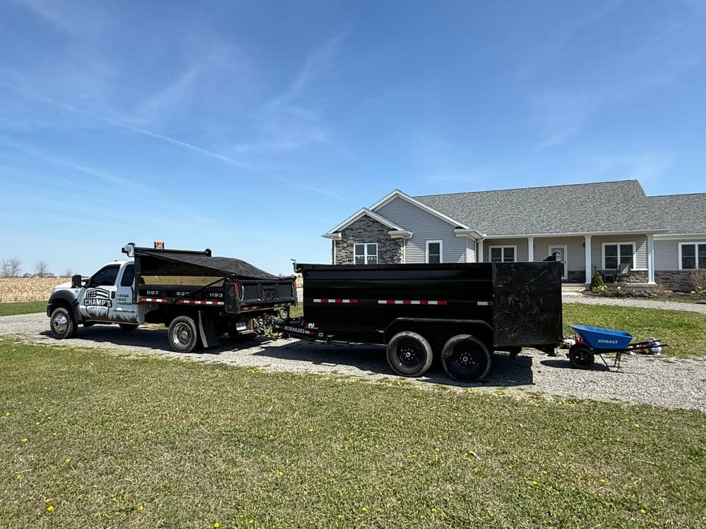 Dump truck and trailer parked at a house, ready for landscaping or construction work.