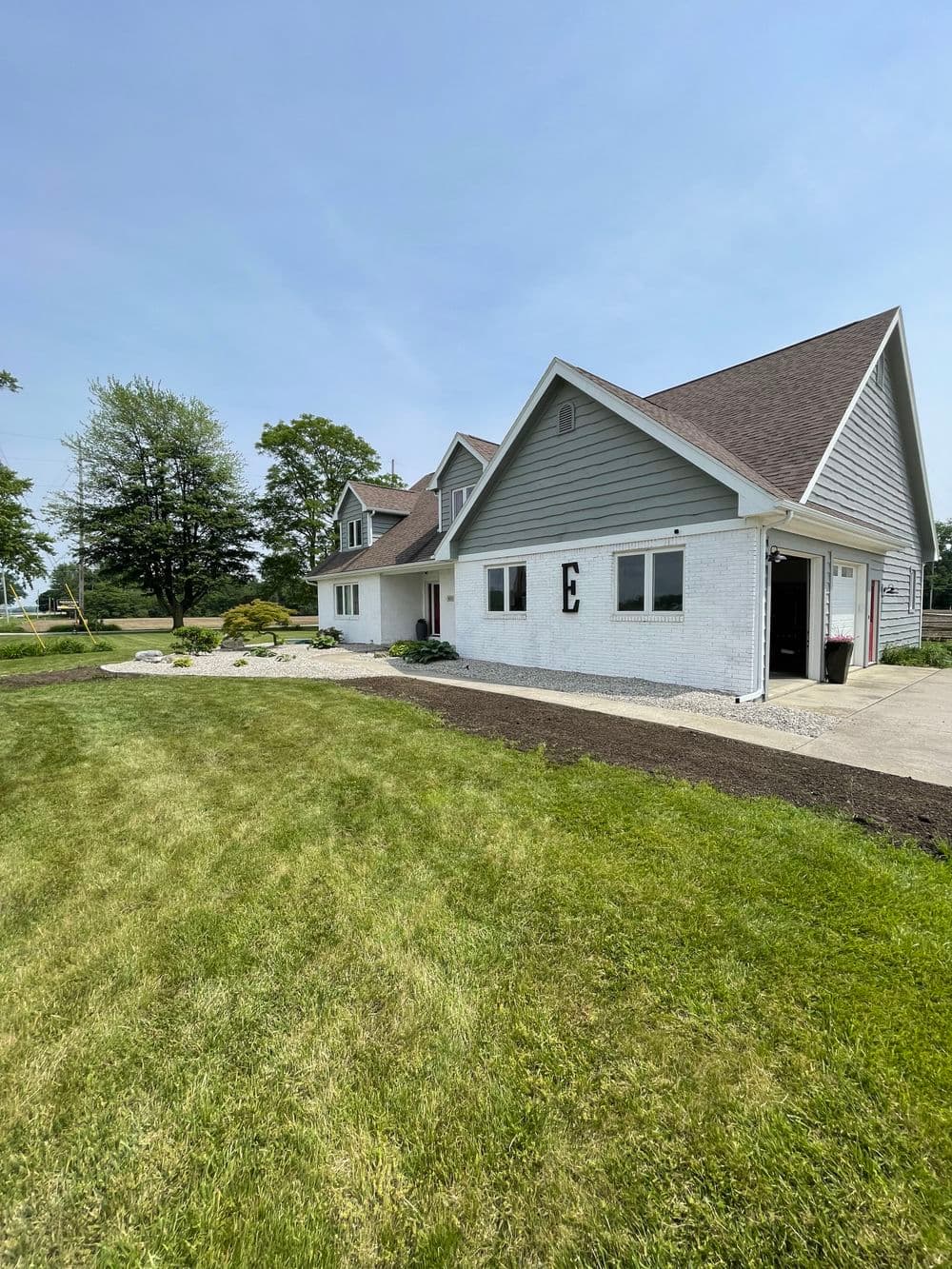Gray and white house with landscaping and lawn under sunny sky. Ideal family home setting.