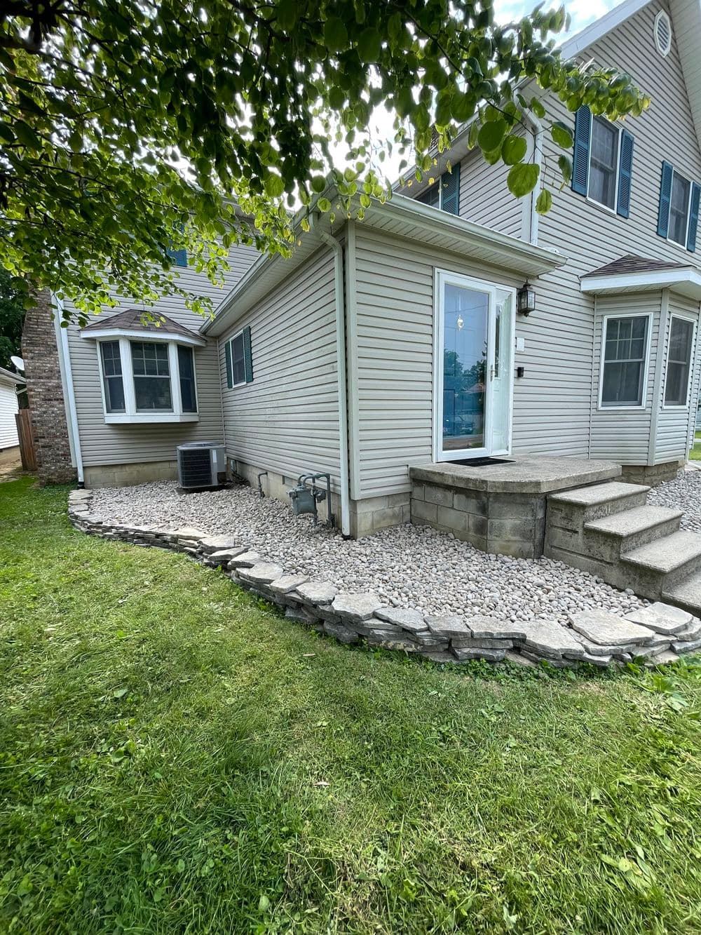 Side view of a two-story house with a landscaped stone path and air conditioning unit.