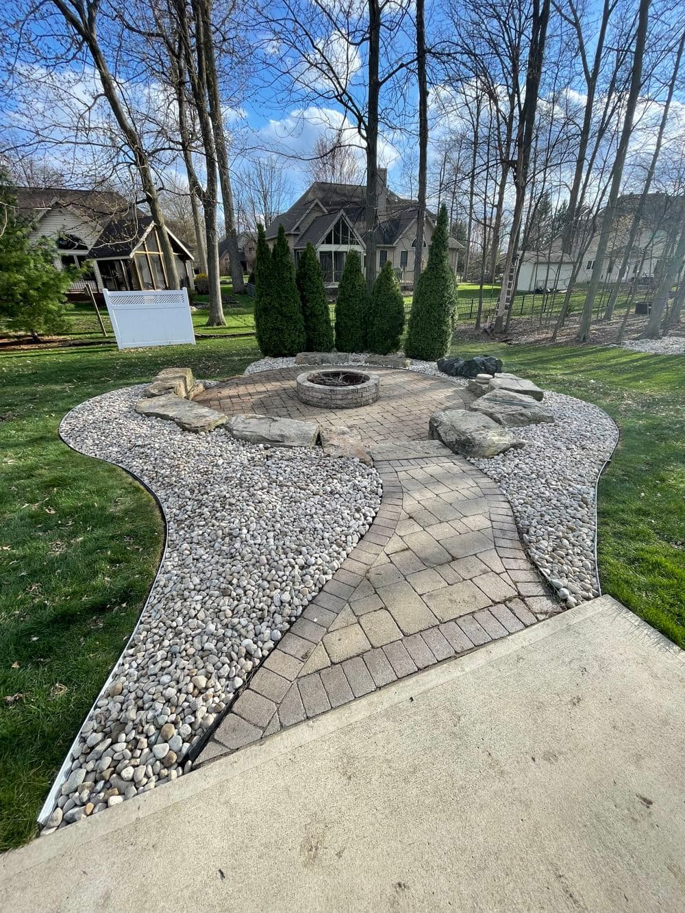 Patio with stone fire pit, landscaped pathways, and ornamental trees in a serene backyard setting.