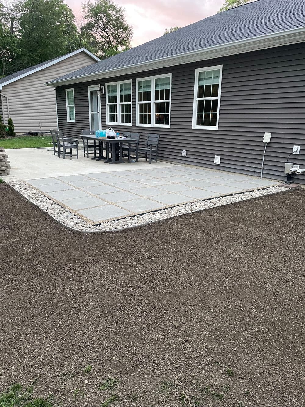Backyard with stone patio, gravel border, and dining set against a modern home exterior.