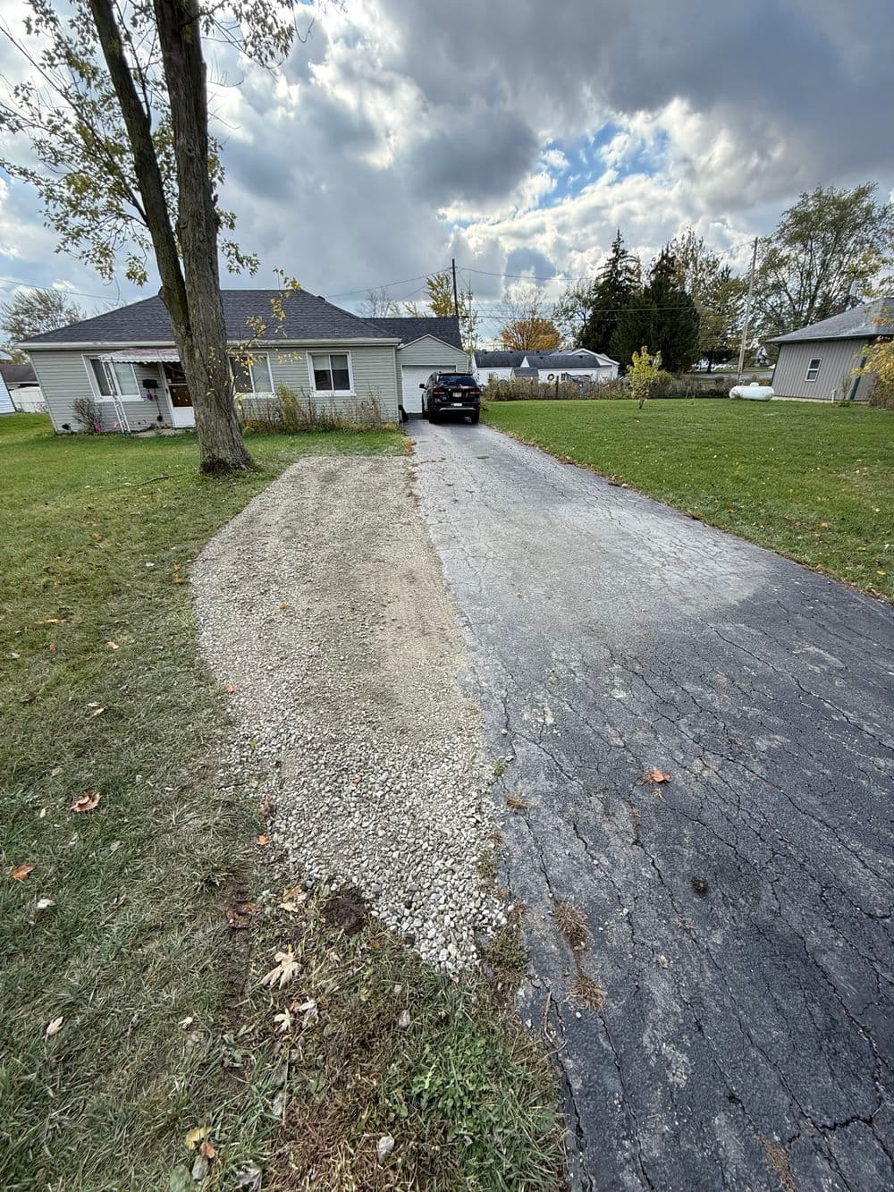 Gravel driveway extension beside a paved driveway leading to a house in a grassy area.