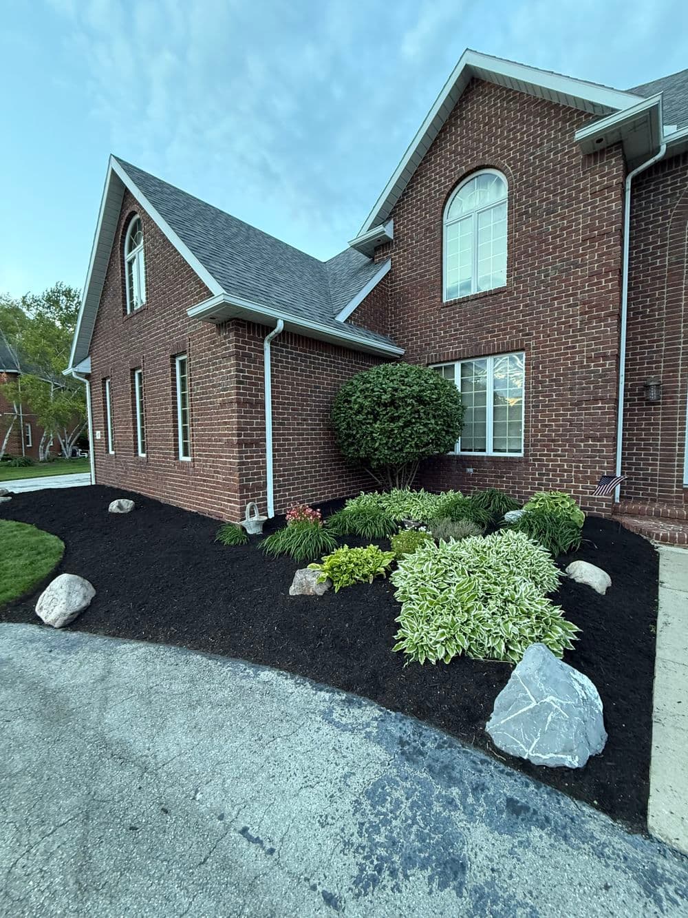 Brick house with lush landscaping and black mulch in front yard.