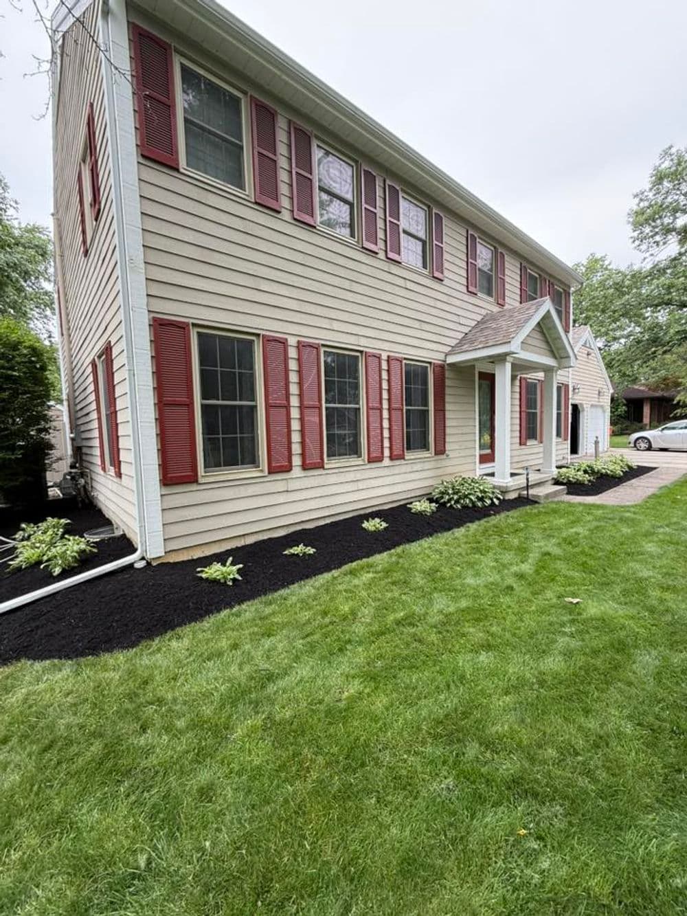Two-story house with red shutters, manicured lawn, and landscaped flower bed.