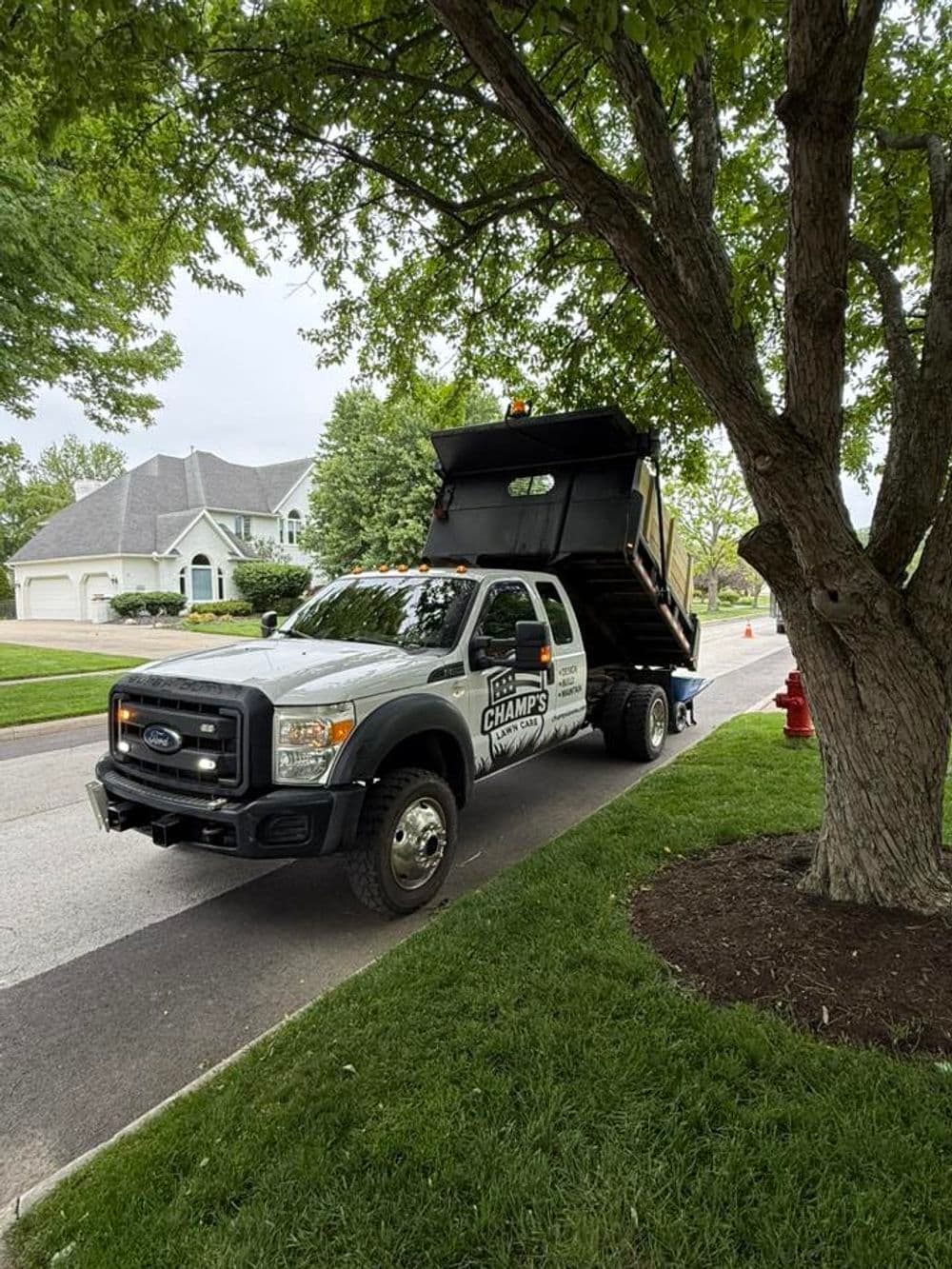 Champs Landscaping dump truck parked on residential street under trees.