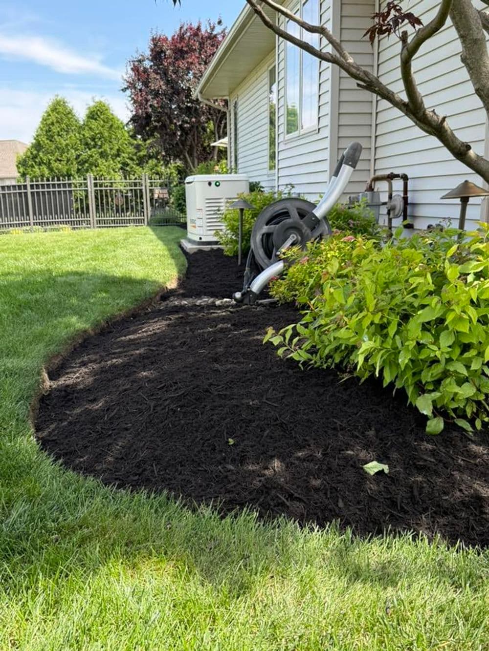 Mulched garden bed with bushes and air conditioning unit alongside a house.