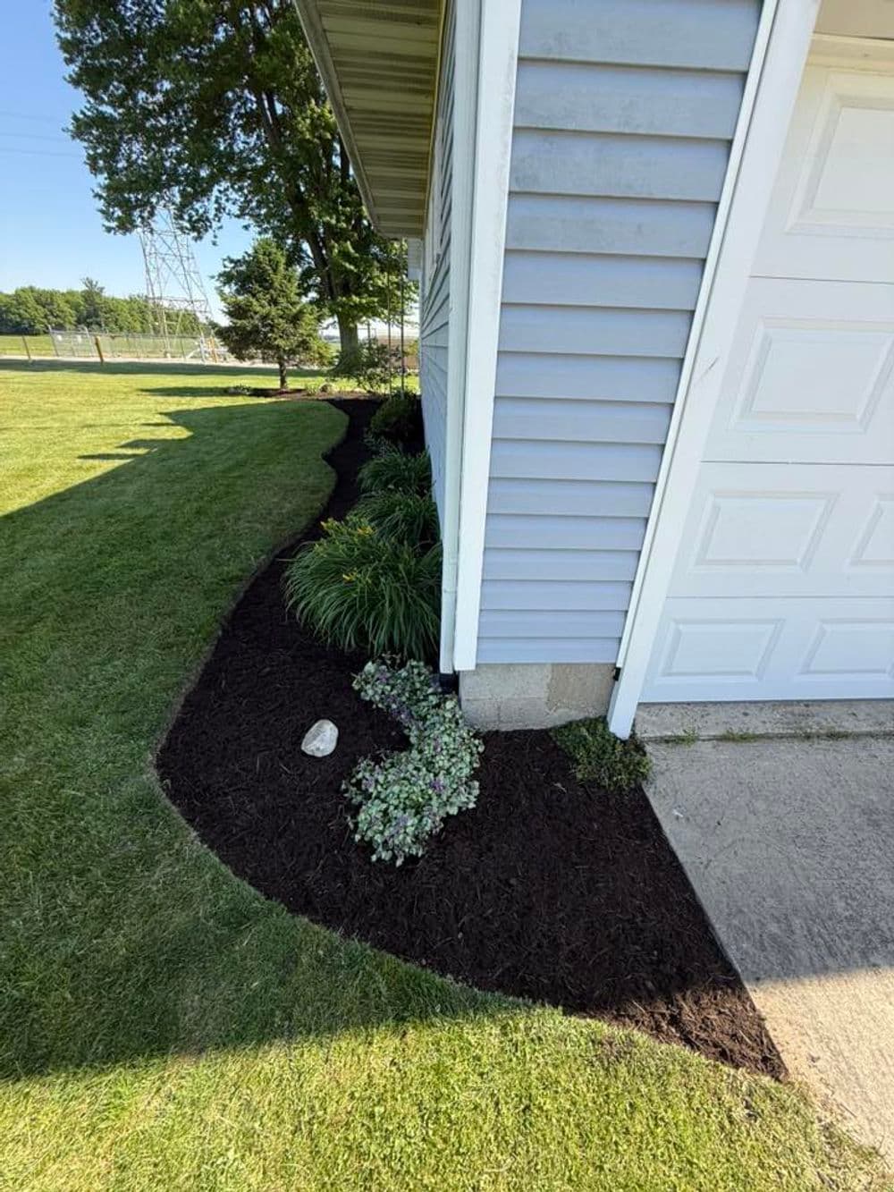 Mulched garden bed around home corner with green plants and landscaping features.