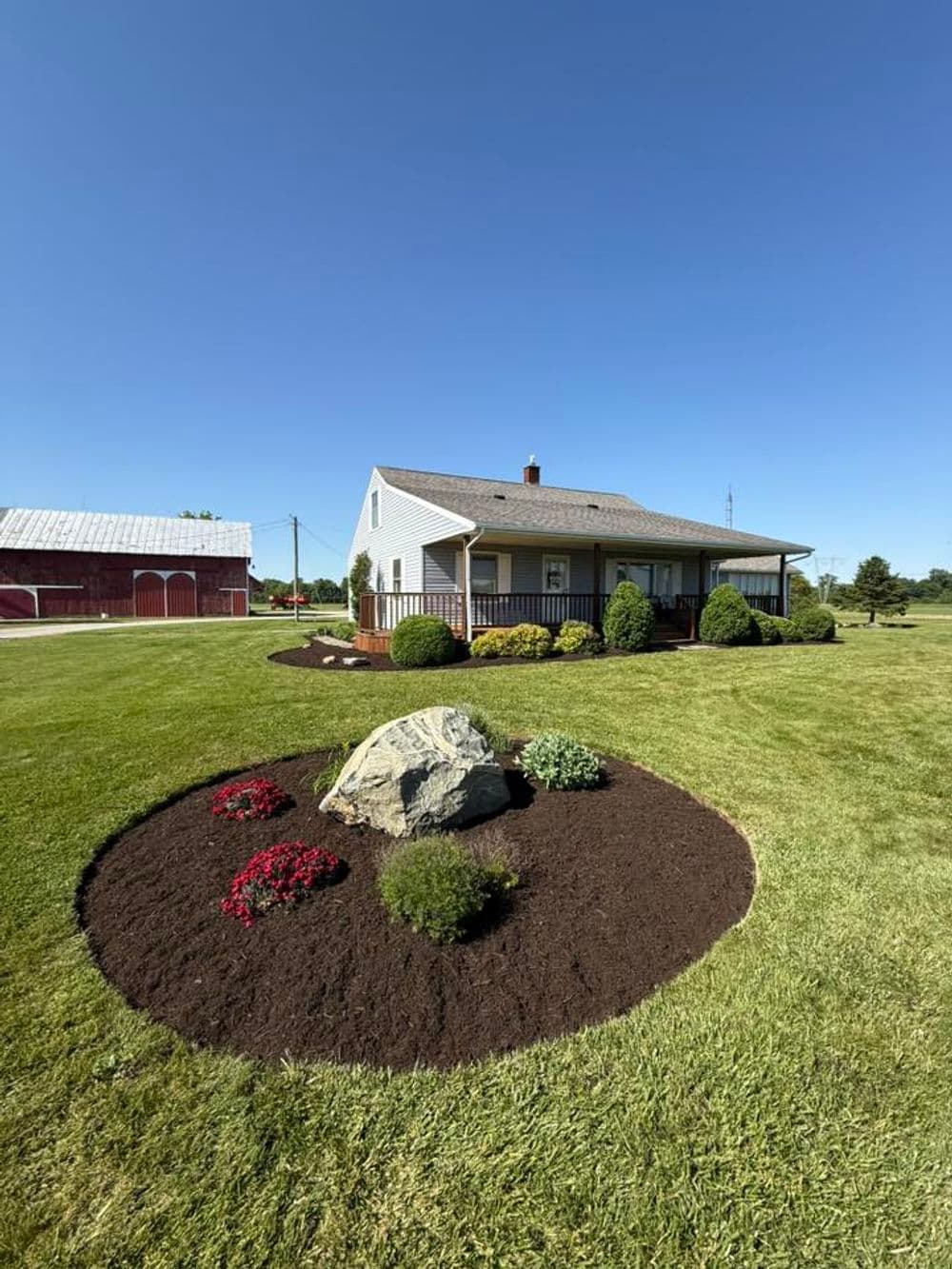 Charming house with landscaped garden, flowers, and a rock in a rural setting.