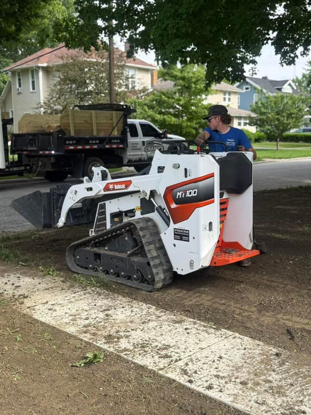 Bobcat MT100 compact track loader in use for landscaping on a residential street.