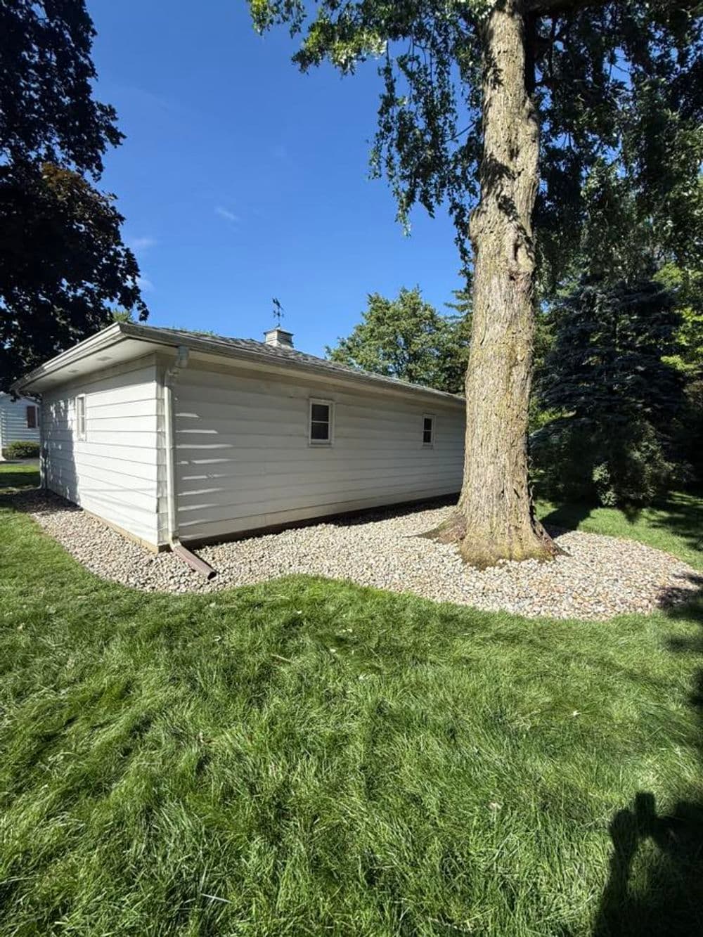 White house exterior with a large tree and landscaped gravel border in a green yard.