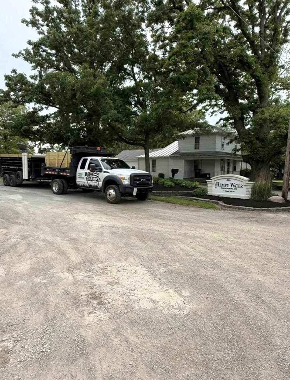 Truck from Happy Water with trailer parked near a large tree and white building.