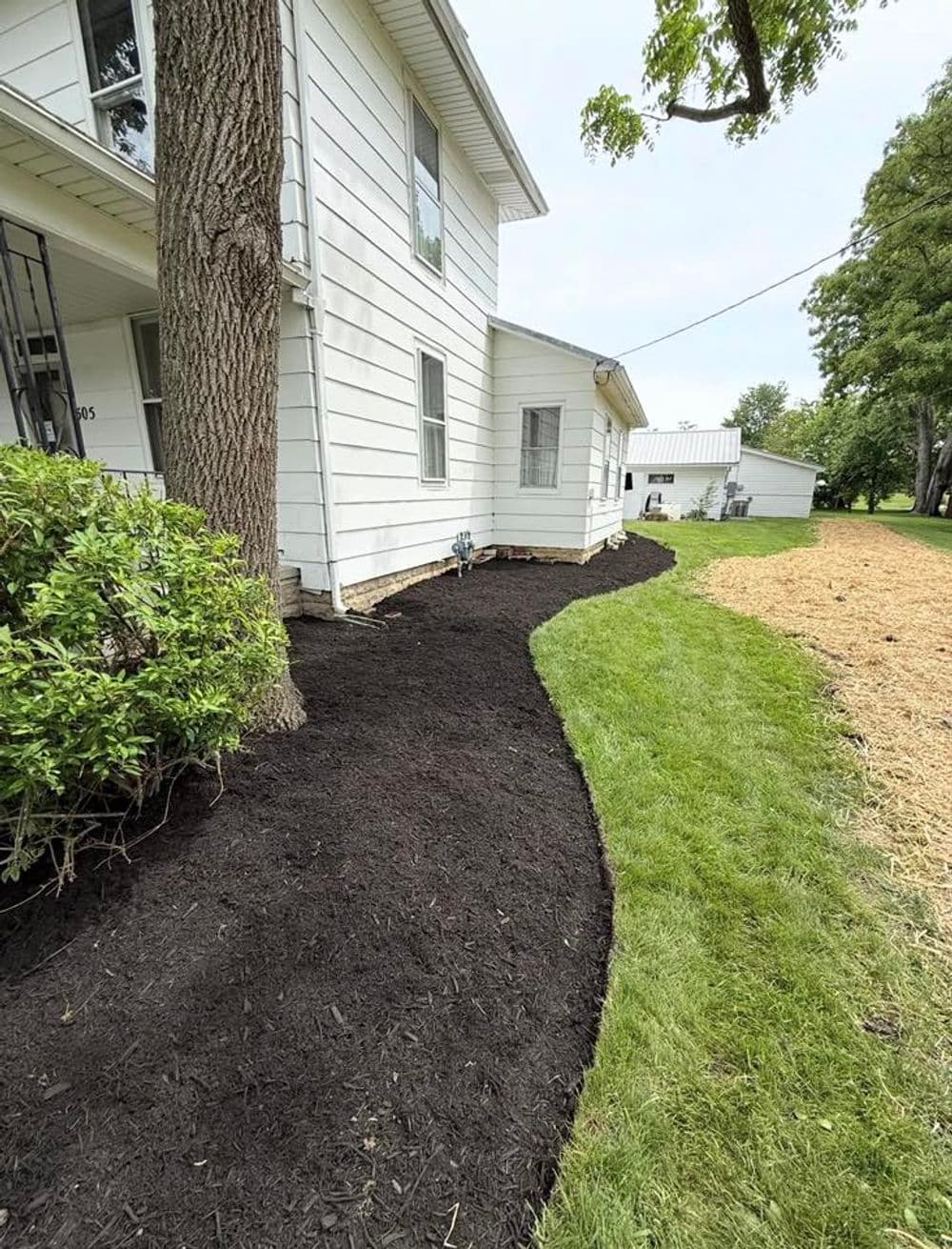 Mulched landscaping along a home's foundation, featuring a curved edge and green grass.