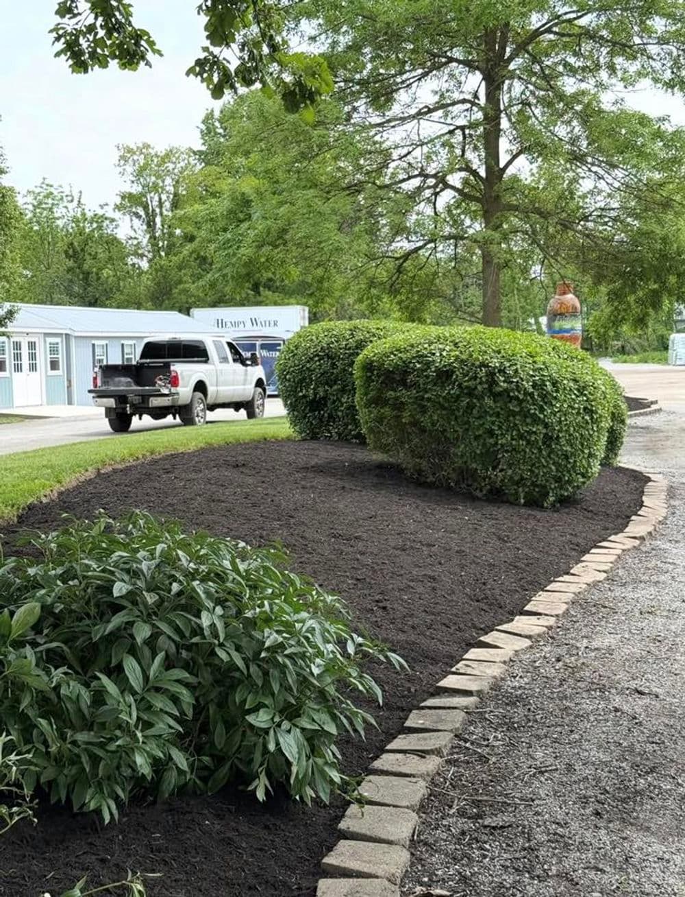 Landscaped garden with shrubs, mulch, and a gravel path near a white pickup truck.