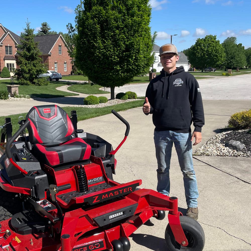 Person giving a thumbs up beside a red Toro Z Master lawn mower in a suburban setting.